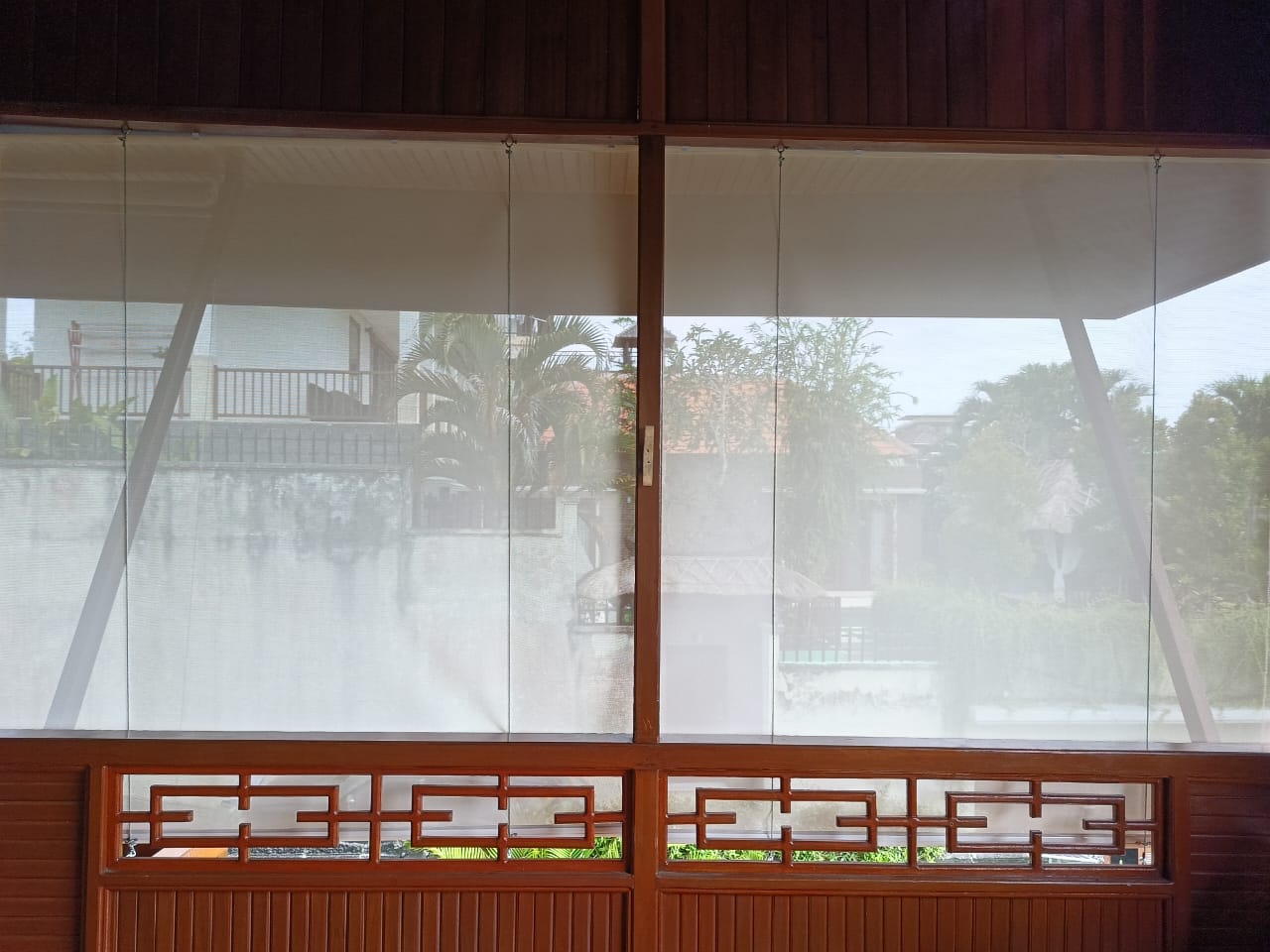 Outdoor roller blinds installed on a patio with sunlight and greenery